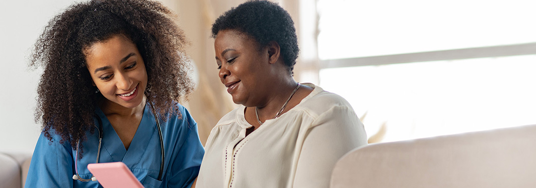 A nurse looking at a tablet with a woman on a couch